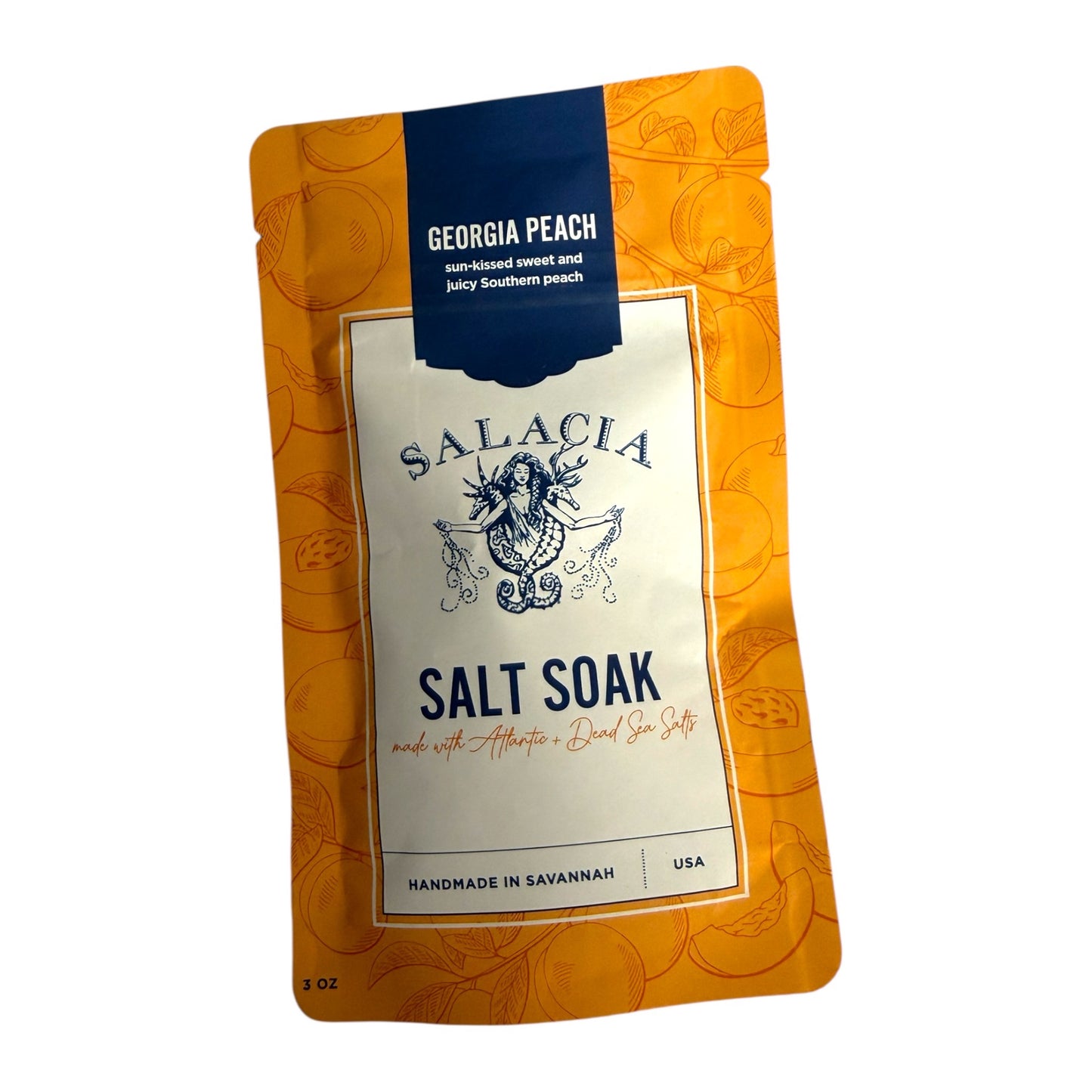 A 2 oz stand-up pouch of Salacia Salt Soak in Georgia Peach flavor, featuring an orange patterned background, a cream central label, and a dark blue top banner.